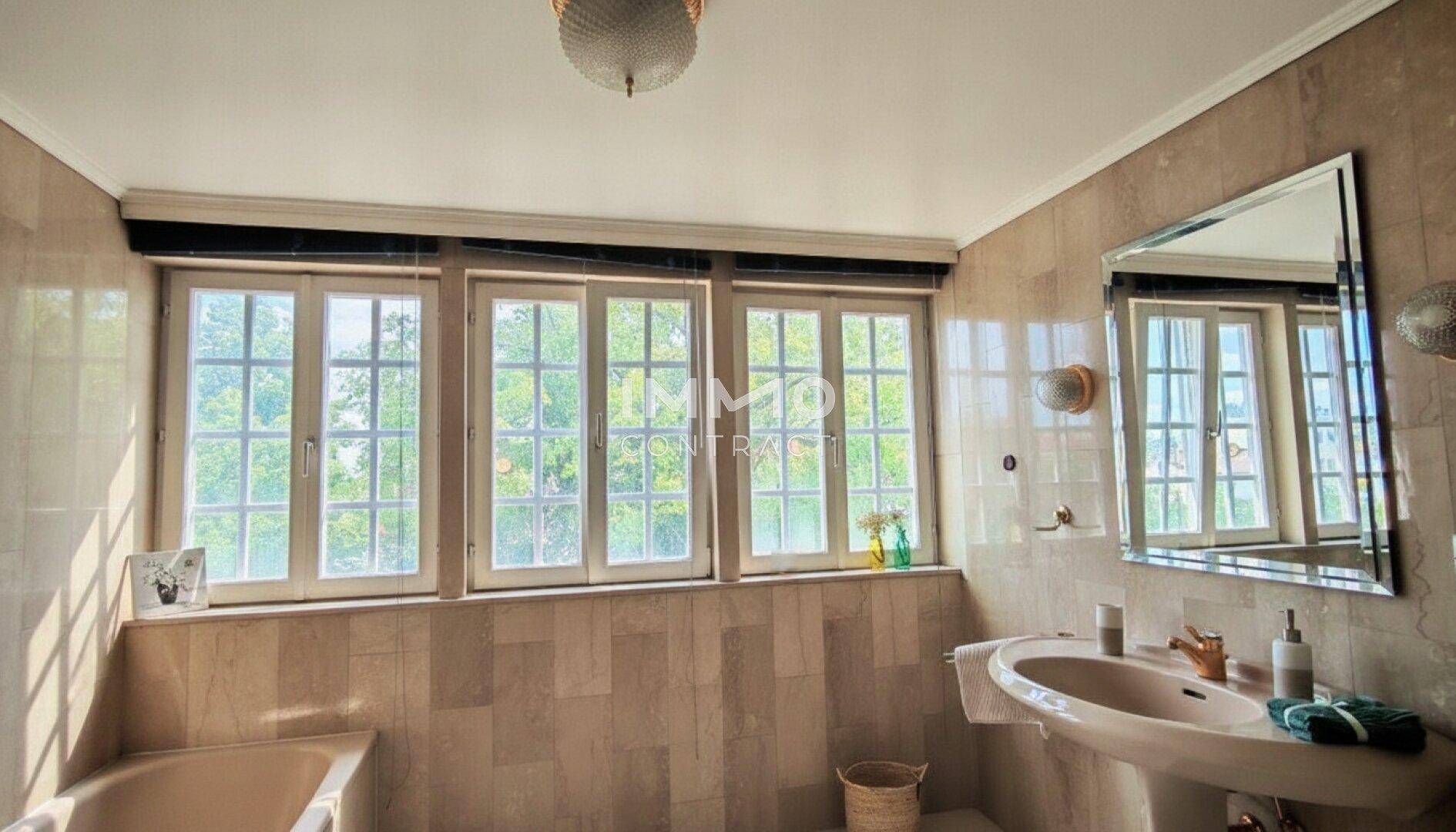 Badezimmer mit gefliesten Wänden und Boden, Waschbecken und Badewanne, hell durch mehrere Fenster.