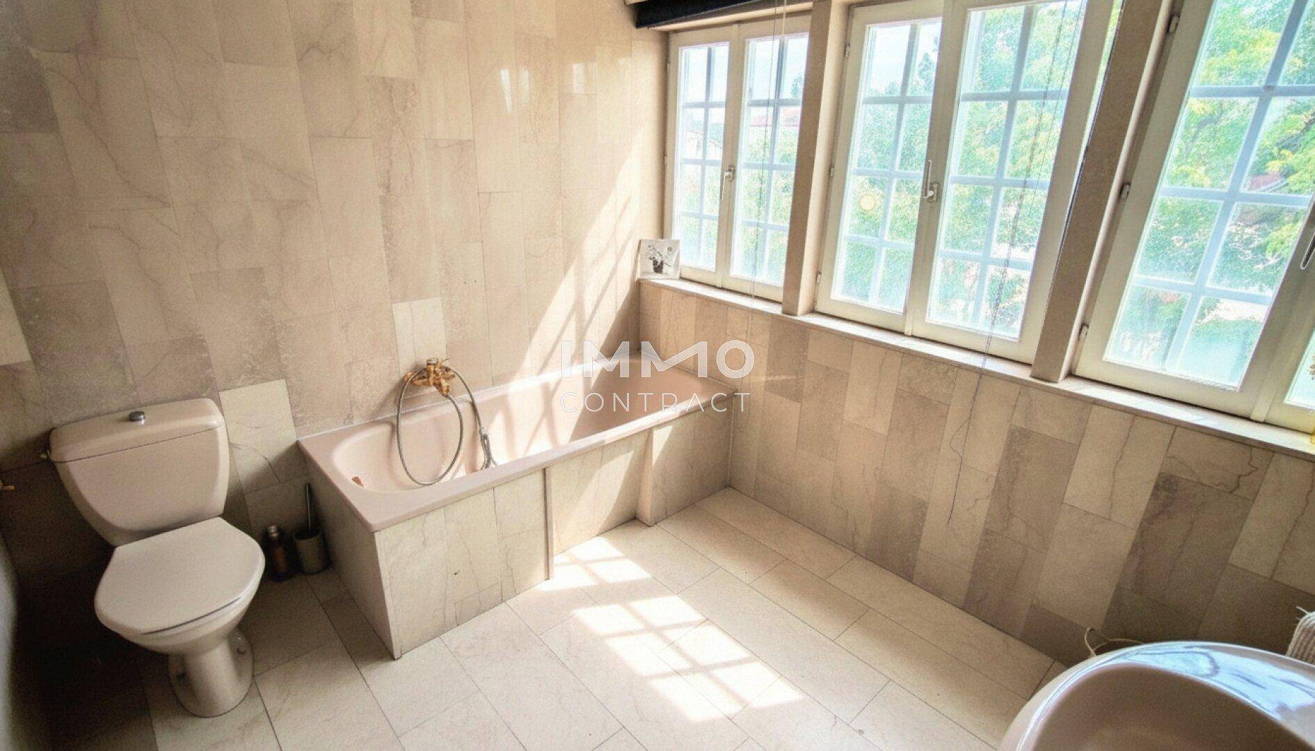 Geräumiges Badezimmer mit Badewanne, Toilette und großen Fenstern, die viel Licht spenden.