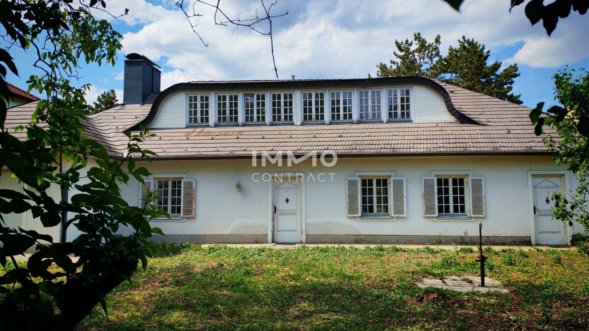 Vorderansicht des Hauses mit markantem Dach und vielen Fenstern, umgeben von einem gepflegten Garten.