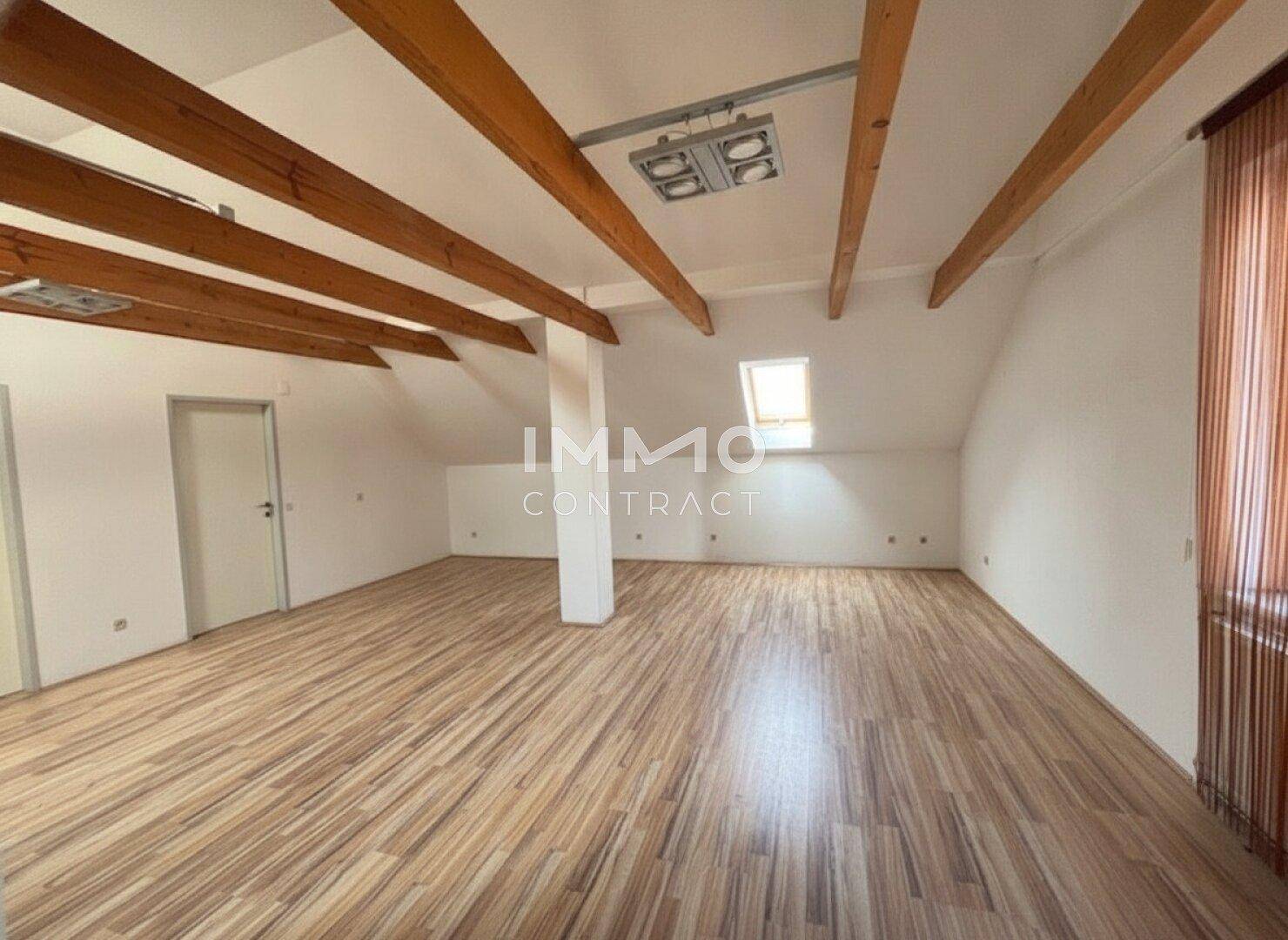 Geräumiger Dachbodenraum mit sichtbaren Holzbalken, Dachfenster und Laminatboden.