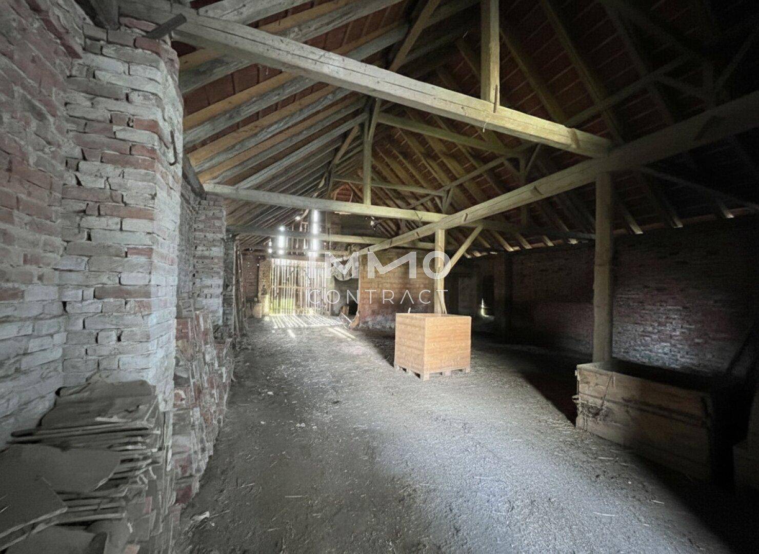 Rustikaler Innenraum einer Scheune mit freiliegenden Holzbalken und Ziegelwänden.