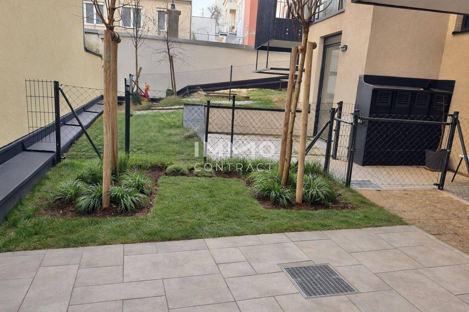 Neu angelegter Gartenbereich mit jungen Bäumen und Rasenfläche, umgeben von einem Zaun.