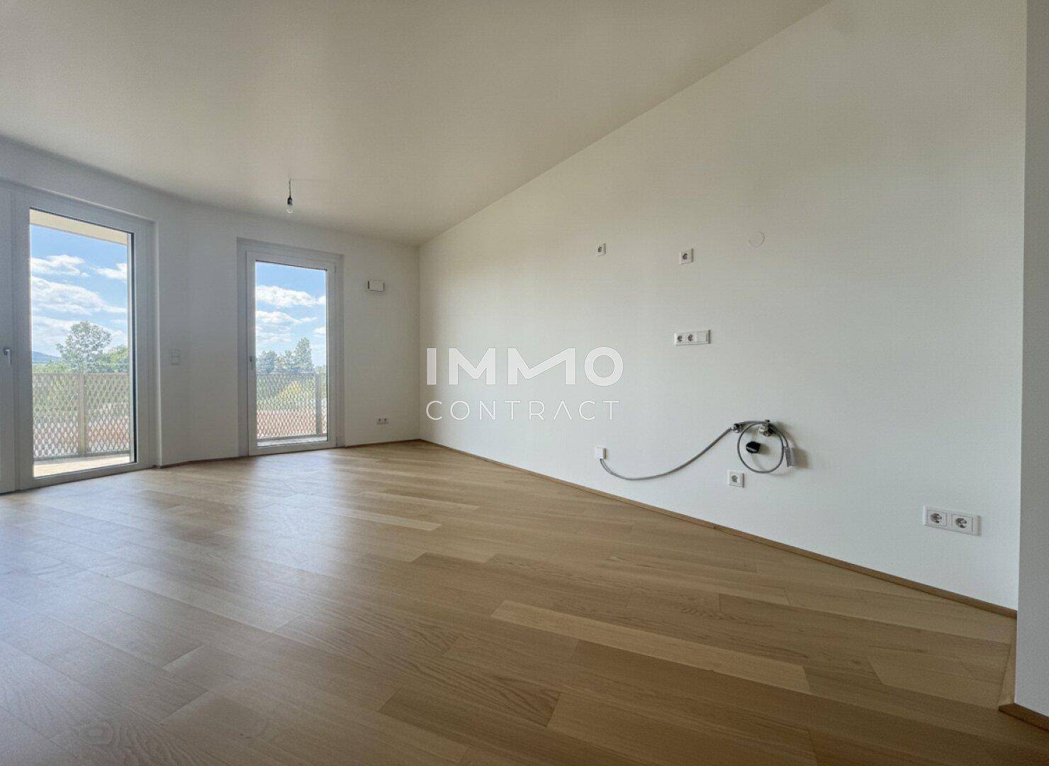 Lichtdurchfluteter Wohnbereich mit hellem Parkettboden und großen Fenstertüren zum Außenbereich.