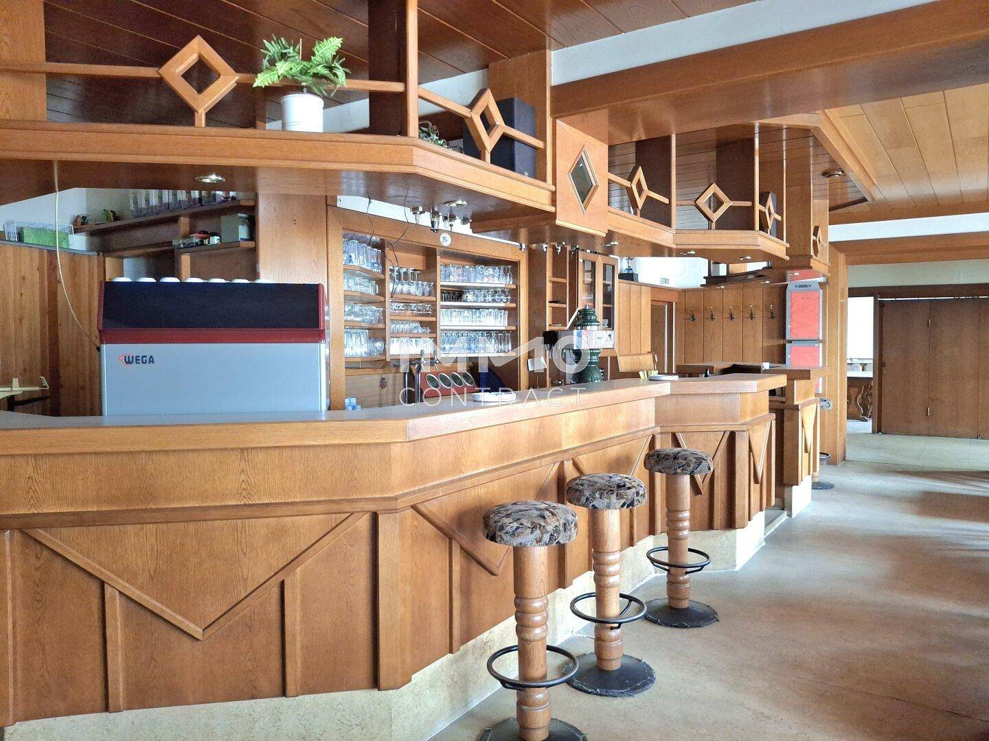Detailansicht der Holzbar mit Barhockern und Gläsern, ausgestattet mit einem Kühlschrank und Dunstabzugshaube.