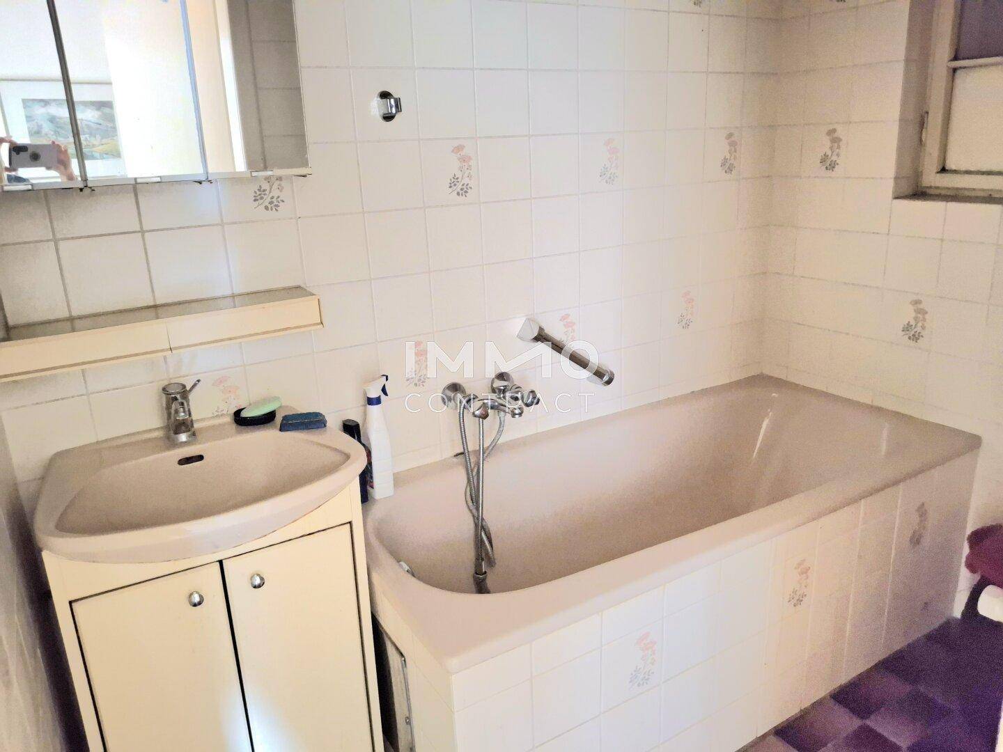 Badezimmer mit Badewanne, Waschbecken und weißen Fliesen mit floralem Muster, funktional und sauber.