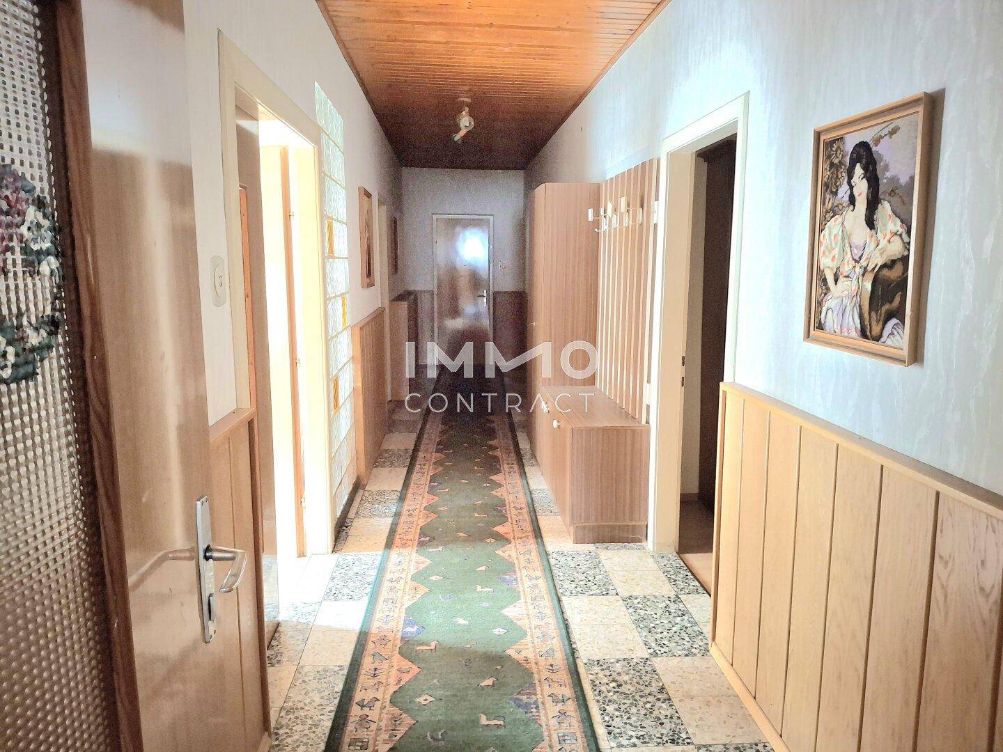 Langer Flur mit Terrazzoboden, Holzvertäfelung und Decken aus Holz, der zu verschiedenen Räumen führt.