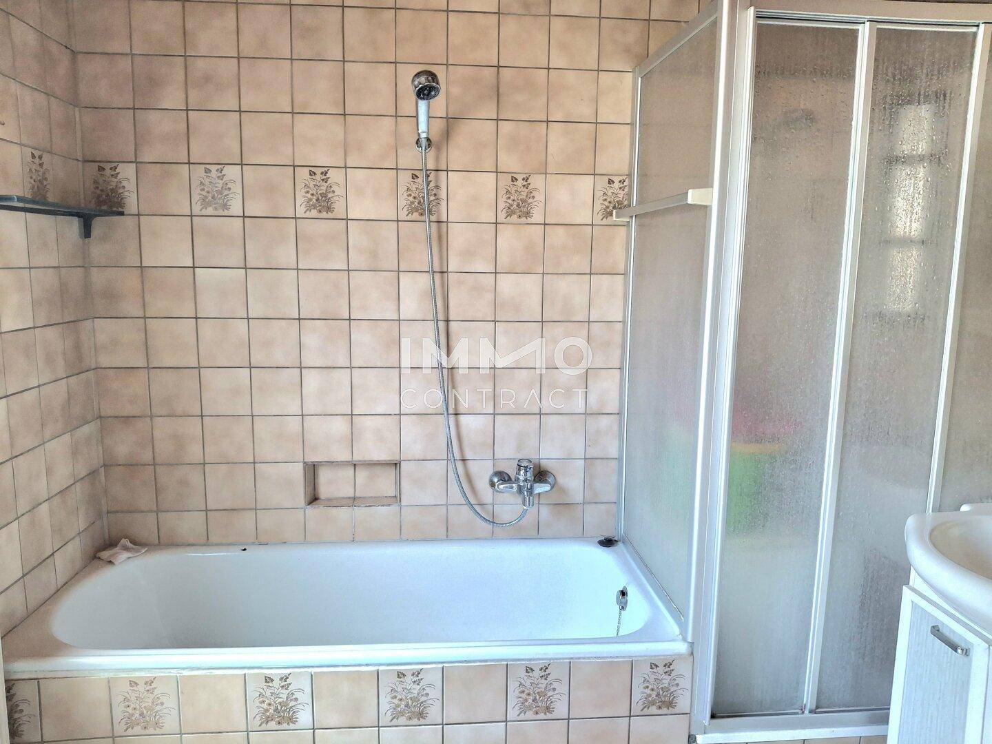 Badezimmer mit Badewanne, Duschkabine und beigefarbenen Fliesen, funktional und gut erhalten.