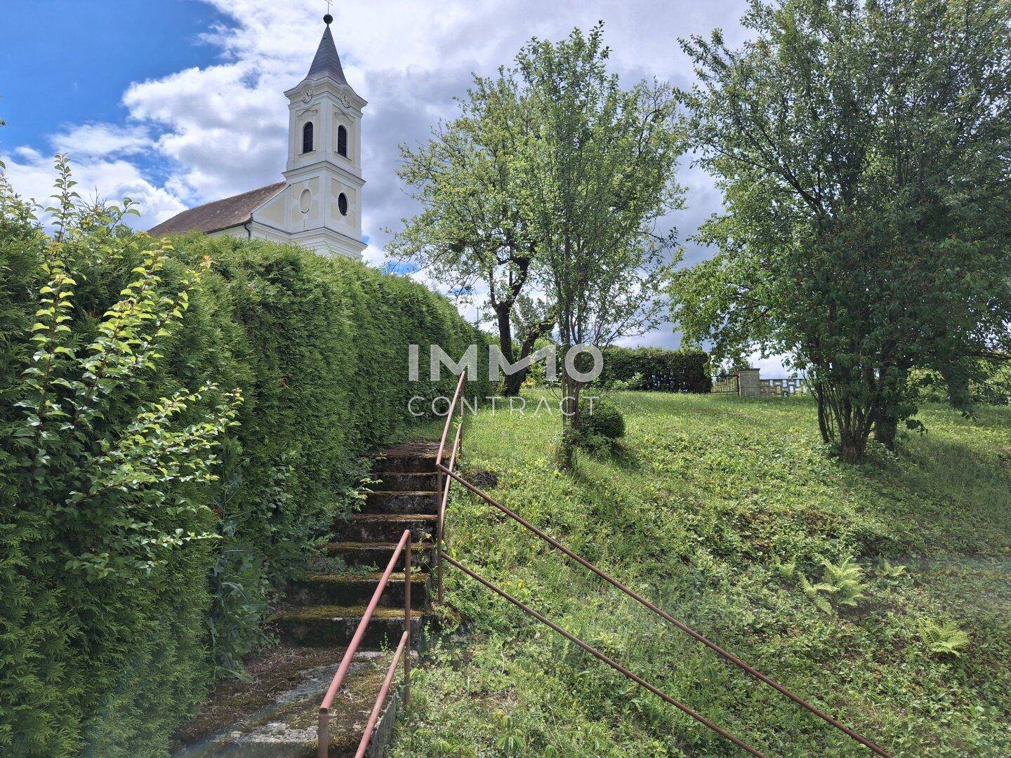 Steintreppe mit Geländer führt einen grünen Hang hinauf zu einer malerischen Kirche.