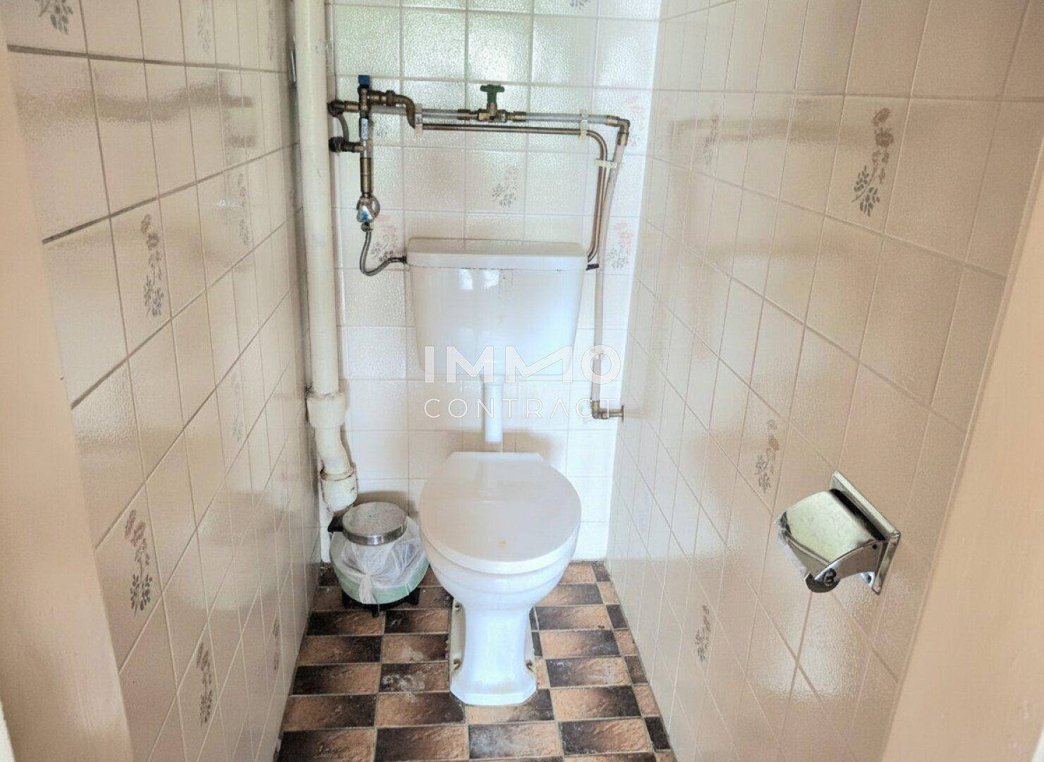 Separate Toilette mit WC, Spülkasten und kariertem Fliesenboden, einfach und praktisch.