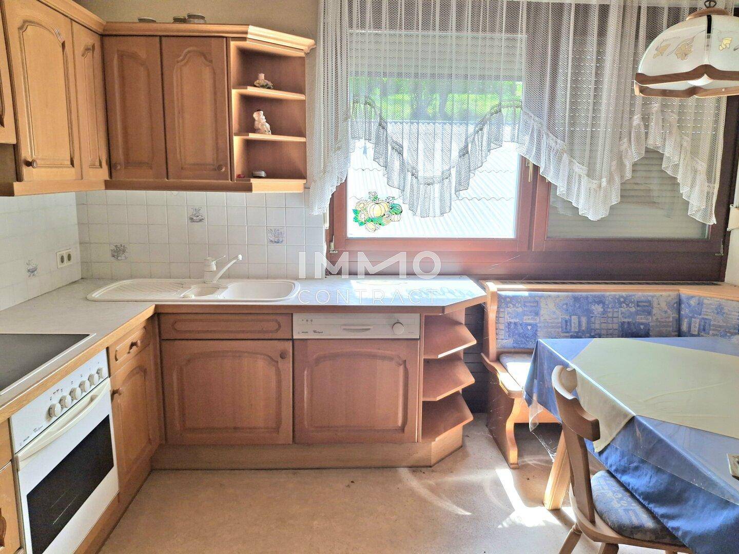 Traditionelle Küche mit Holzschränken, Spülmaschine und einem Essbereich am Fenster, hell und funktional.