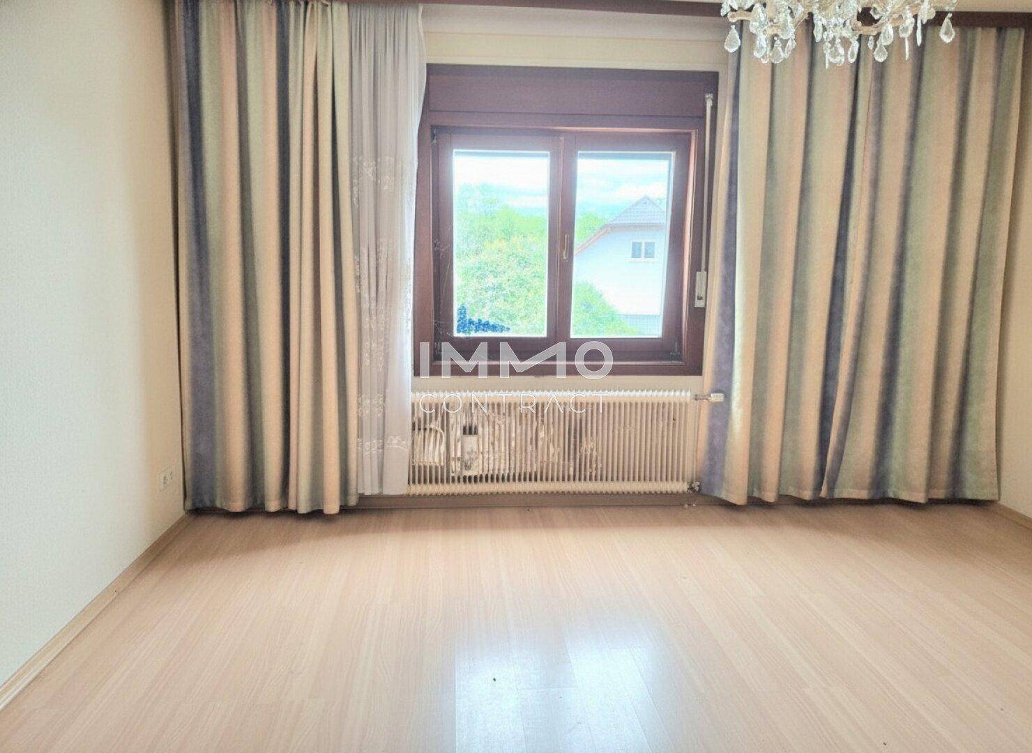 Helles Schlafzimmer mit Laminatboden, großem Fenster und Vorhängen, bietet eine angenehme Atmosphäre.