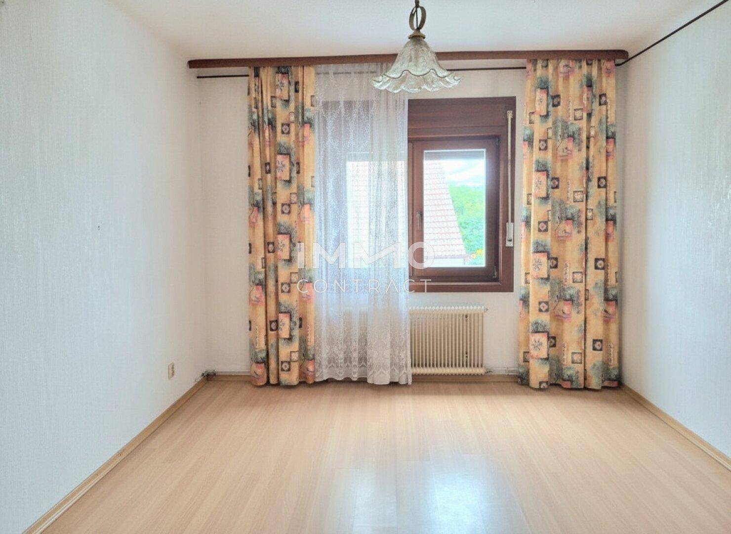 Schlafzimmer mit Laminatboden, Fenster und gemusterten Vorhängen, bietet einen Blick ins Grüne.