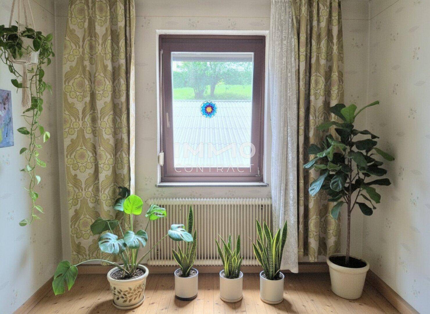Schlafzimmer mit Holzdielenboden, Fenster und vielen Zimmerpflanzen, die eine frische Atmosphäre schaffen.