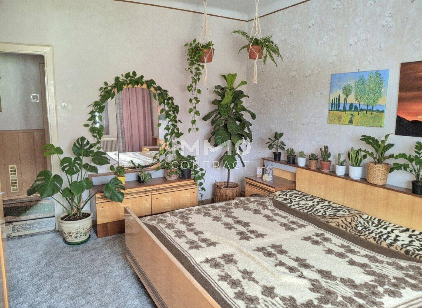 Schlafzimmer mit Teppichboden, Doppelbett und vielen Zimmerpflanzen, die eine gemütliche Atmosphäre schaffen.