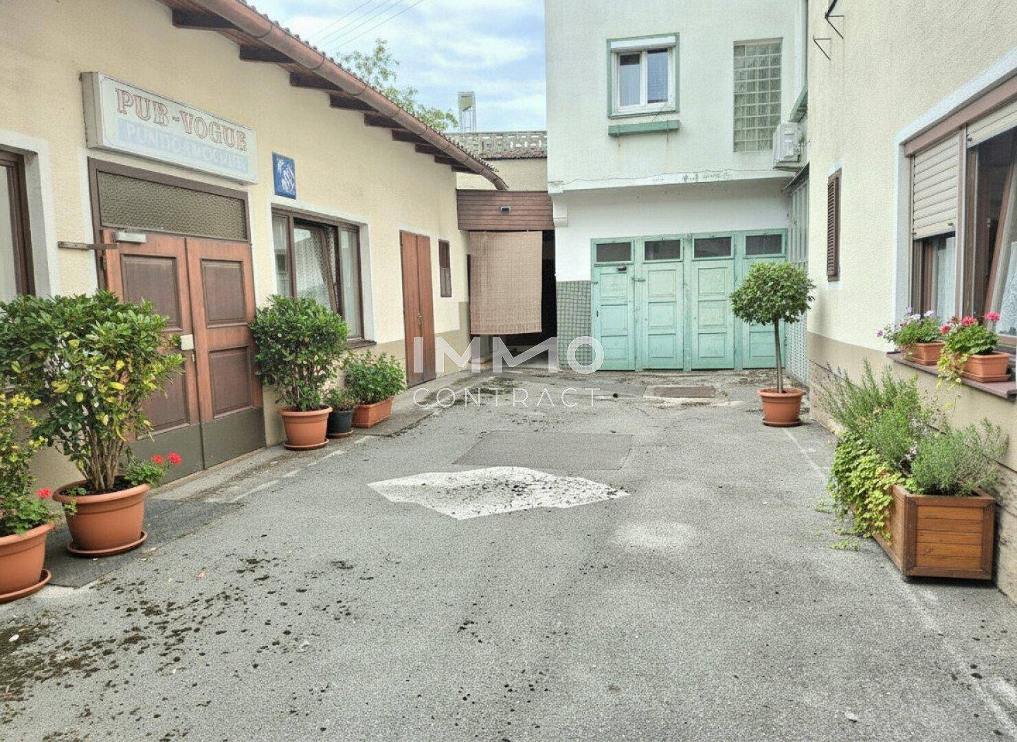 Enge Gasse zwischen Gebäuden mit Topfpflanzen und einem alten Garagentor.