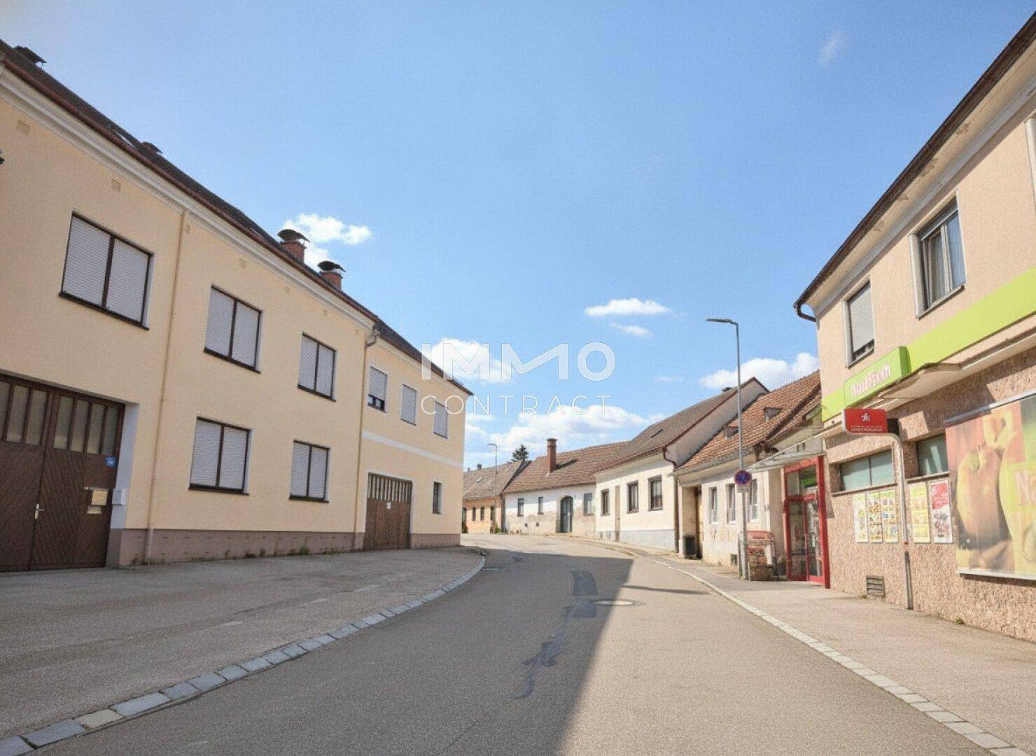 Ruhige Dorfstraße mit traditionellen Gebäuden unter einem klaren blauen Himmel.