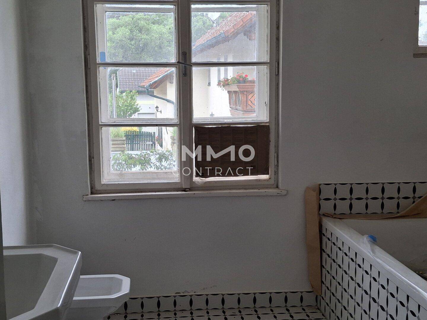 Badezimmer mit Badewanne, Toilette und Fenster, das einen Blick nach draußen bietet.