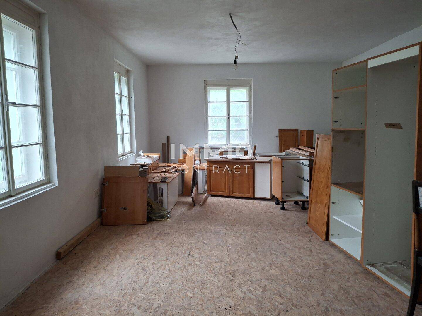 Renovierungsbedürftige Küche mit vorbereiteten Schränken und zwei großen Fenstern.