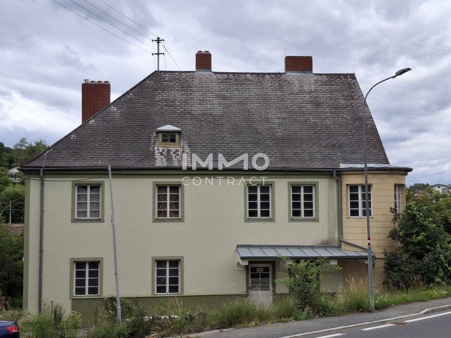 Historisches Gebäude von der Straße aus gesehen, mit Mansarddach und grüner Umgebung.