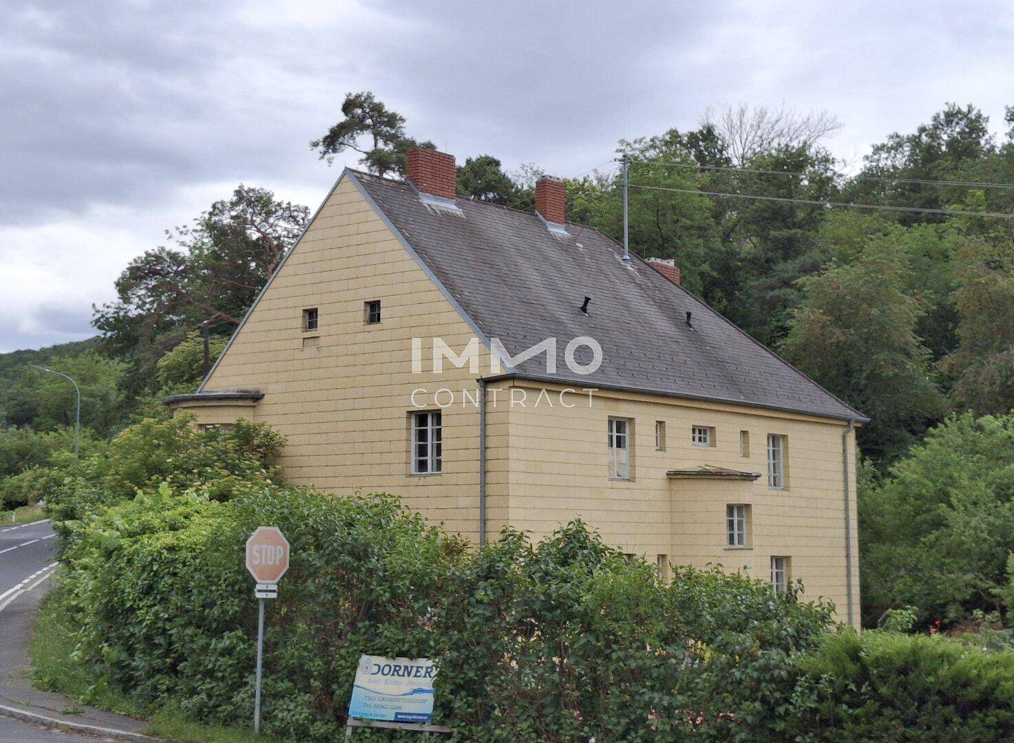Seitenansicht des historischen Gebäudes mit gelber Fassade und umgebender Natur.