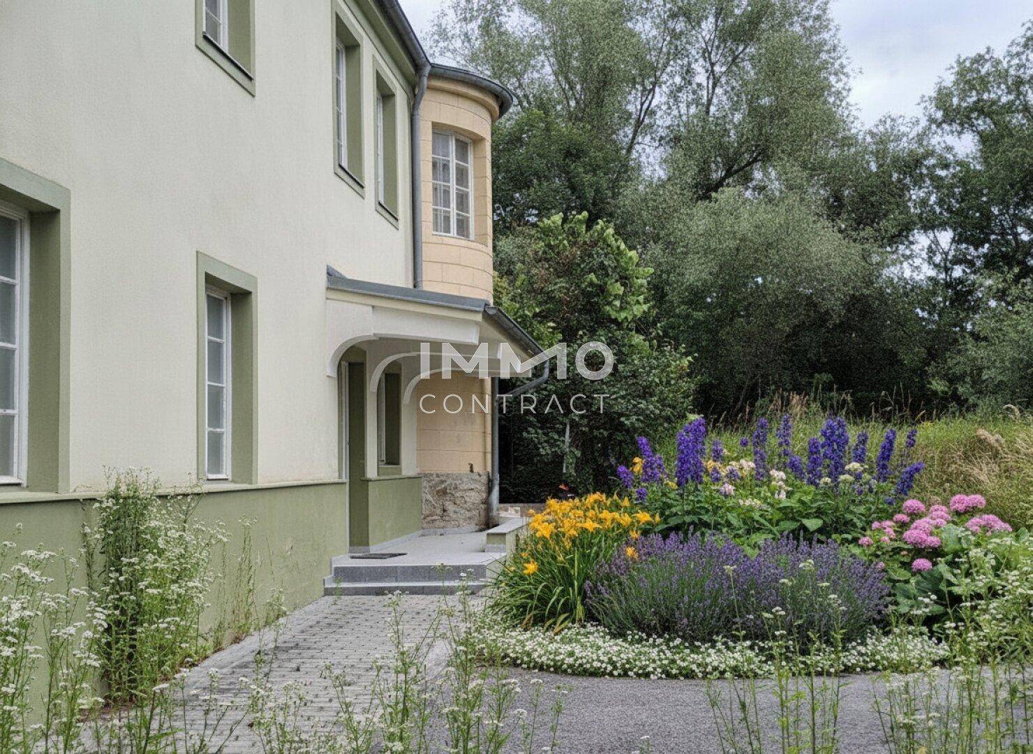 Eingangsbereich des Hauses mit gepflastertem Weg und farbenfrohen Blumenbeeten.