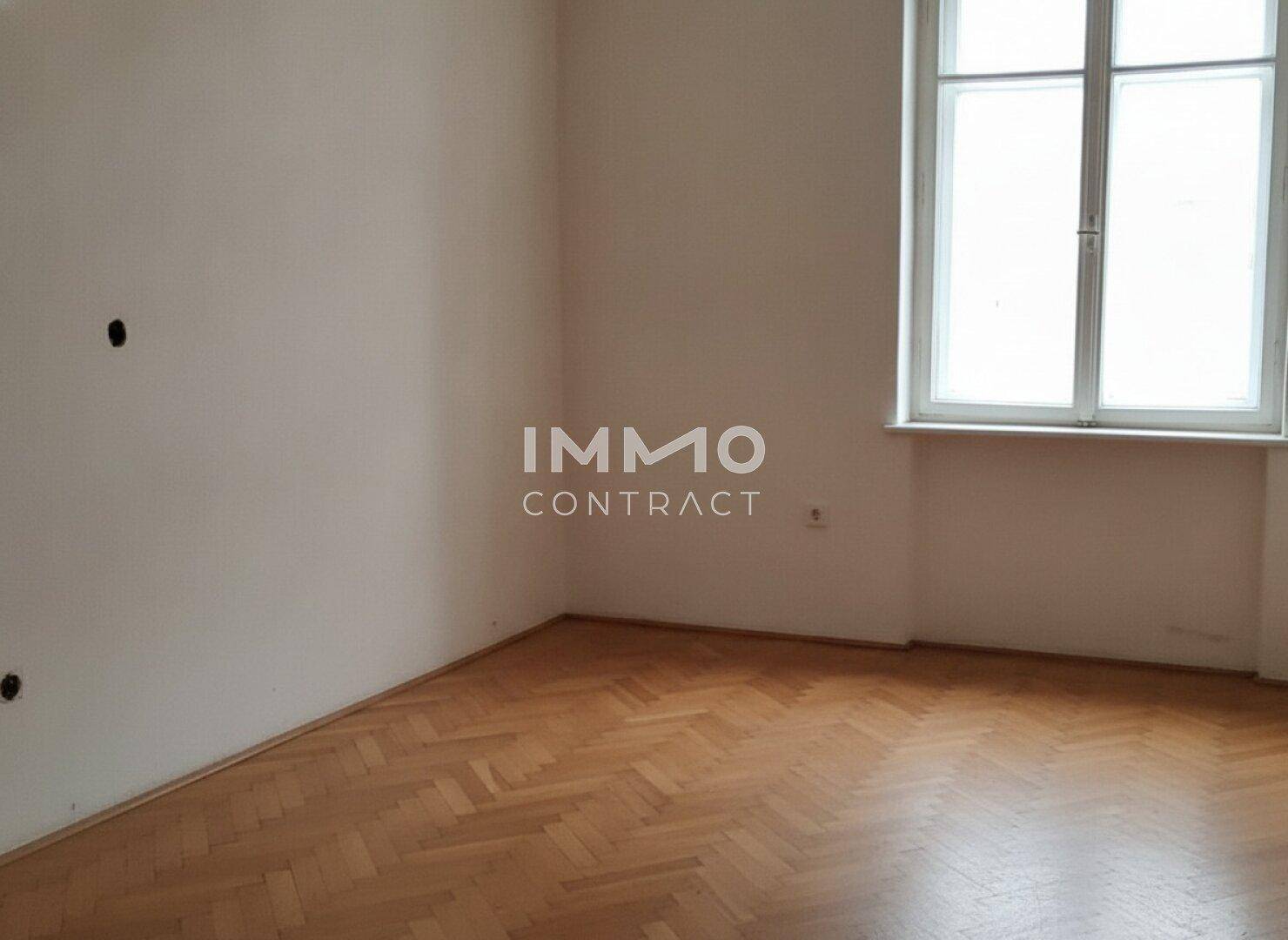 Leeres Schlafzimmer mit Fischgrätparkett und einem großen Fenster, ideal für individuelle Einrichtung.