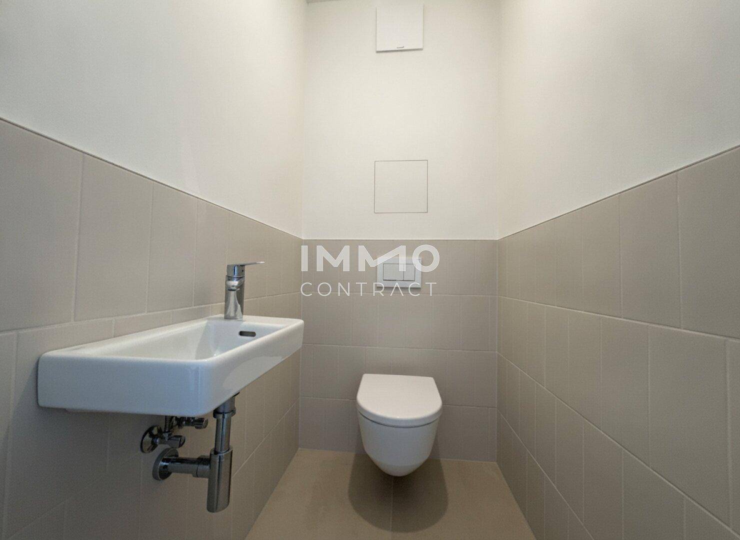 Gäste-WC mit wandhängender Toilette, kleinem Waschbecken und hellen Wandfliesen.