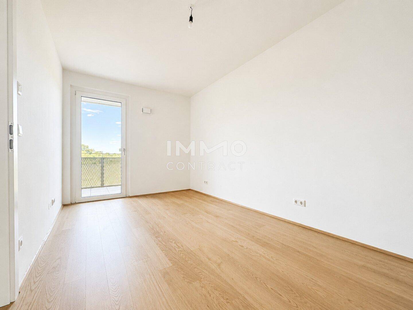 Leeres Schlafzimmer mit hellem Parkettboden und direktem Zugang zu einem Balkon.