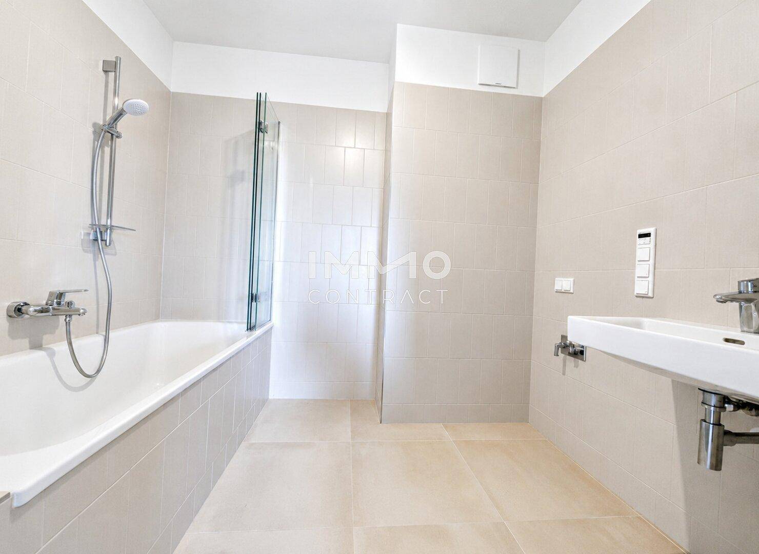 Modernes Badezimmer mit Badewanne, Duscharmatur, Waschbecken und hellen Fliesen.