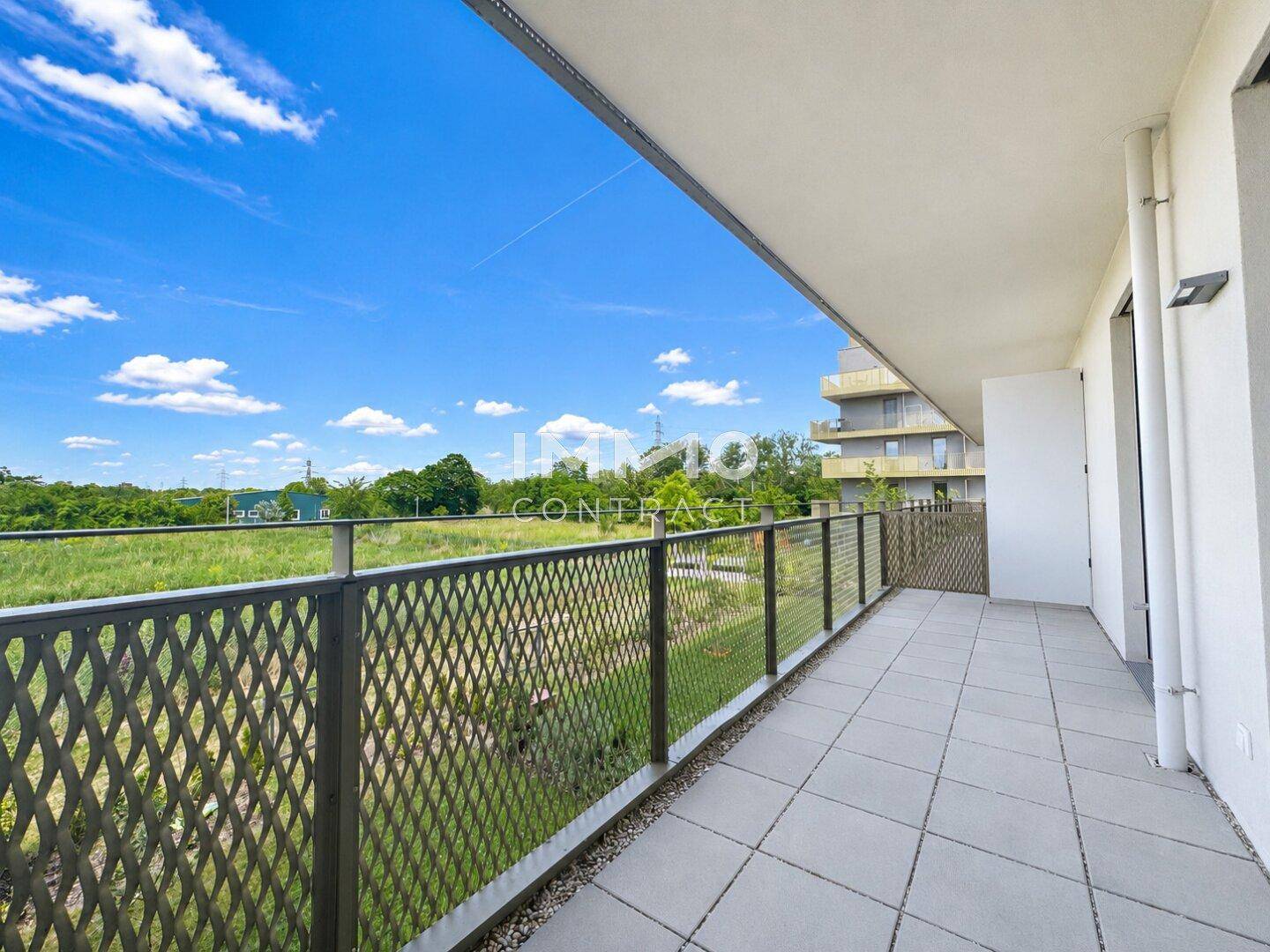 Geräumiger Balkon mit Fliesenboden und weitem Blick ins Grüne unter blauem Himmel.