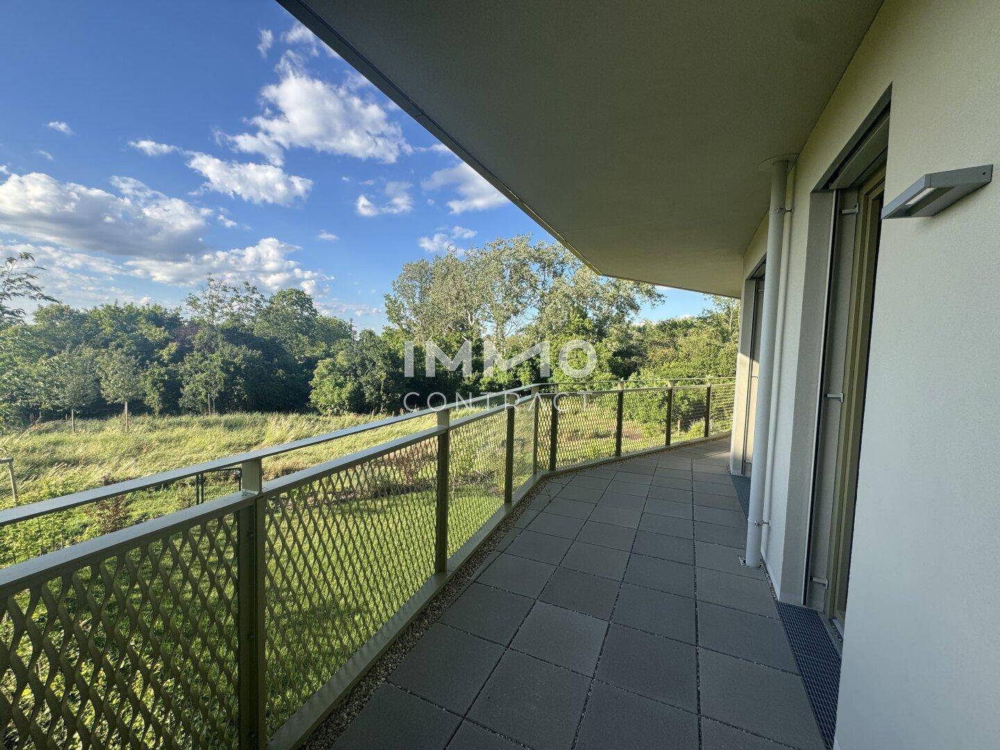 Langer, geschwungener Balkon mit Fliesenboden und weitem Blick ins Grüne unter blauem Himmel.