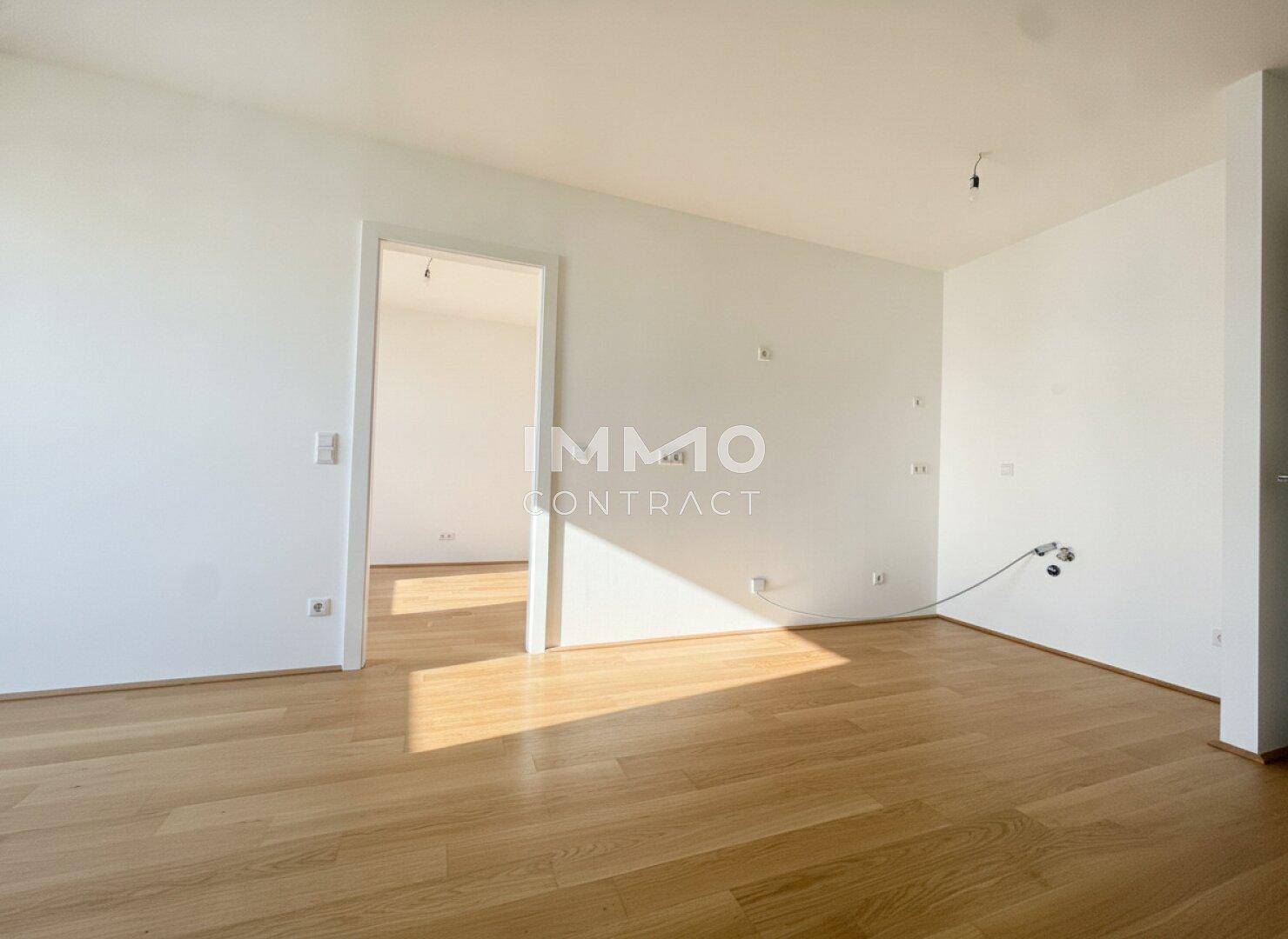 Heller, leerer Raum mit Holzboden und offenem Durchgang zu einem weiteren Zimmer.