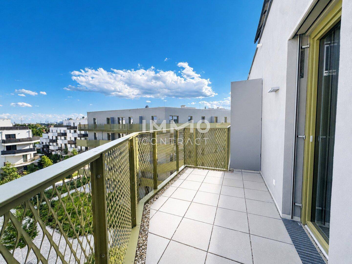Geräumiger Balkon mit Fliesenboden und Blick auf die moderne Wohnanlage und Grünflächen.