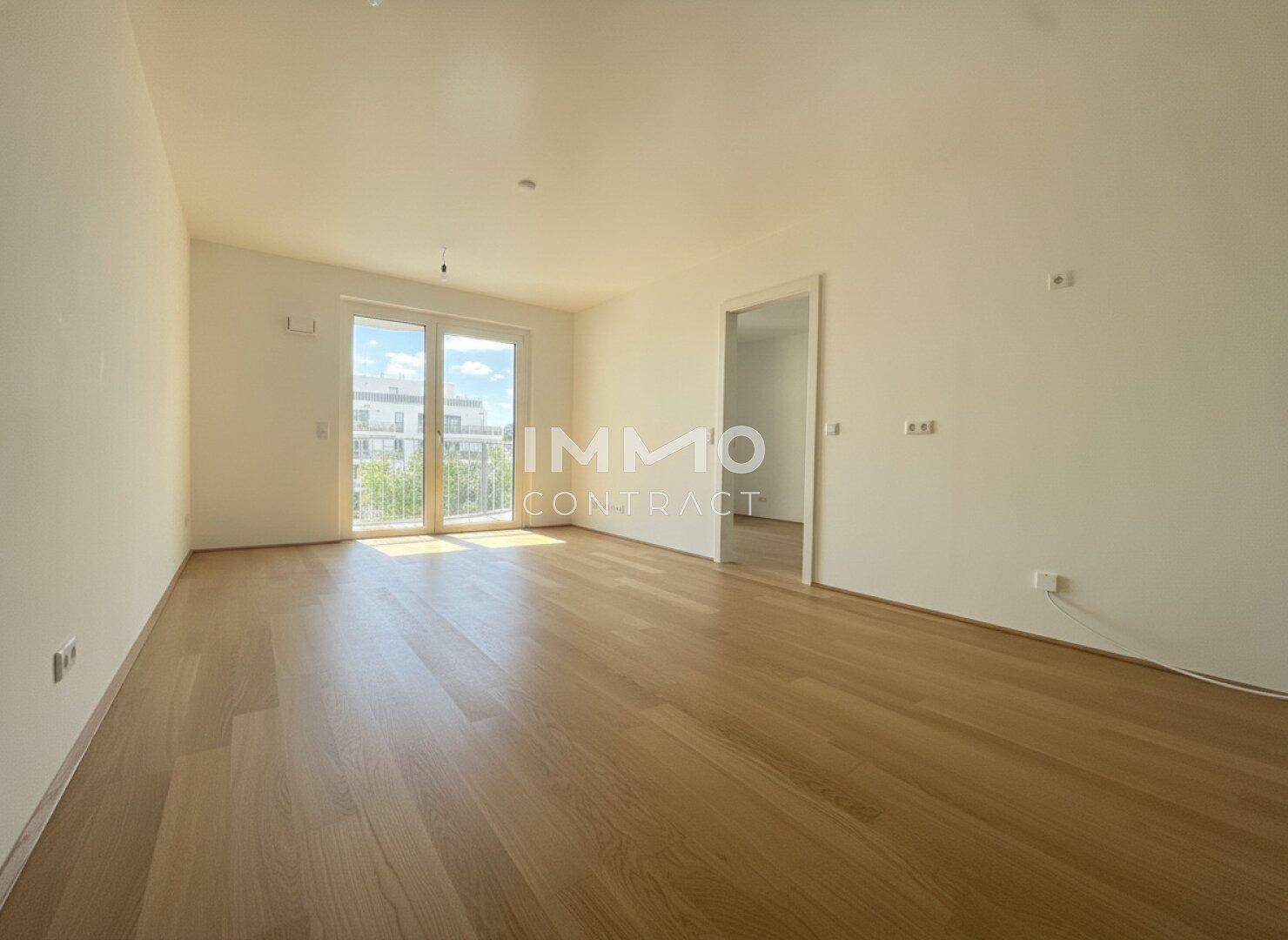 Heller, leerer Raum mit Holzboden und Zugang zu einem Balkon, ideal als Wohnzimmer.