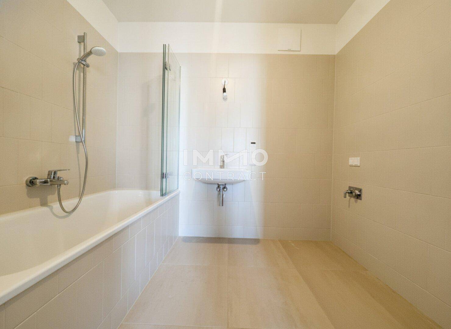 Modernes Badezimmer mit Badewanne, Duschvorrichtung und hellem Fliesenboden.