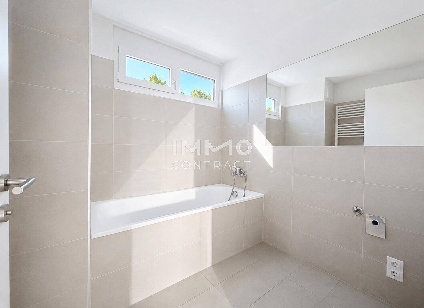 Modernes Badezimmer mit Badewanne, großen Fliesen und einem Fenster für natürliche Belüftung.
