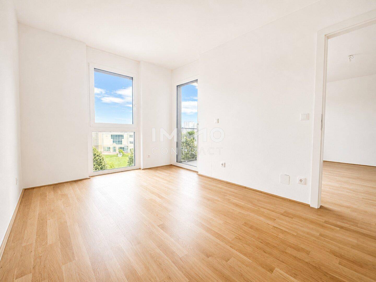 Lichtdurchflutetes Zimmer mit Parkettboden und großen Fenstern, die einen grünen Ausblick bieten.