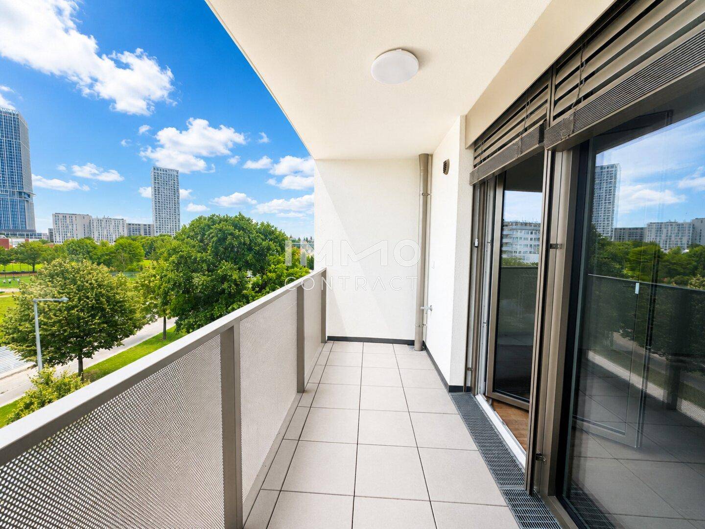 Moderner Balkon mit Fliesenboden und Blick auf die Stadt sowie eine grüne Parkanlage.