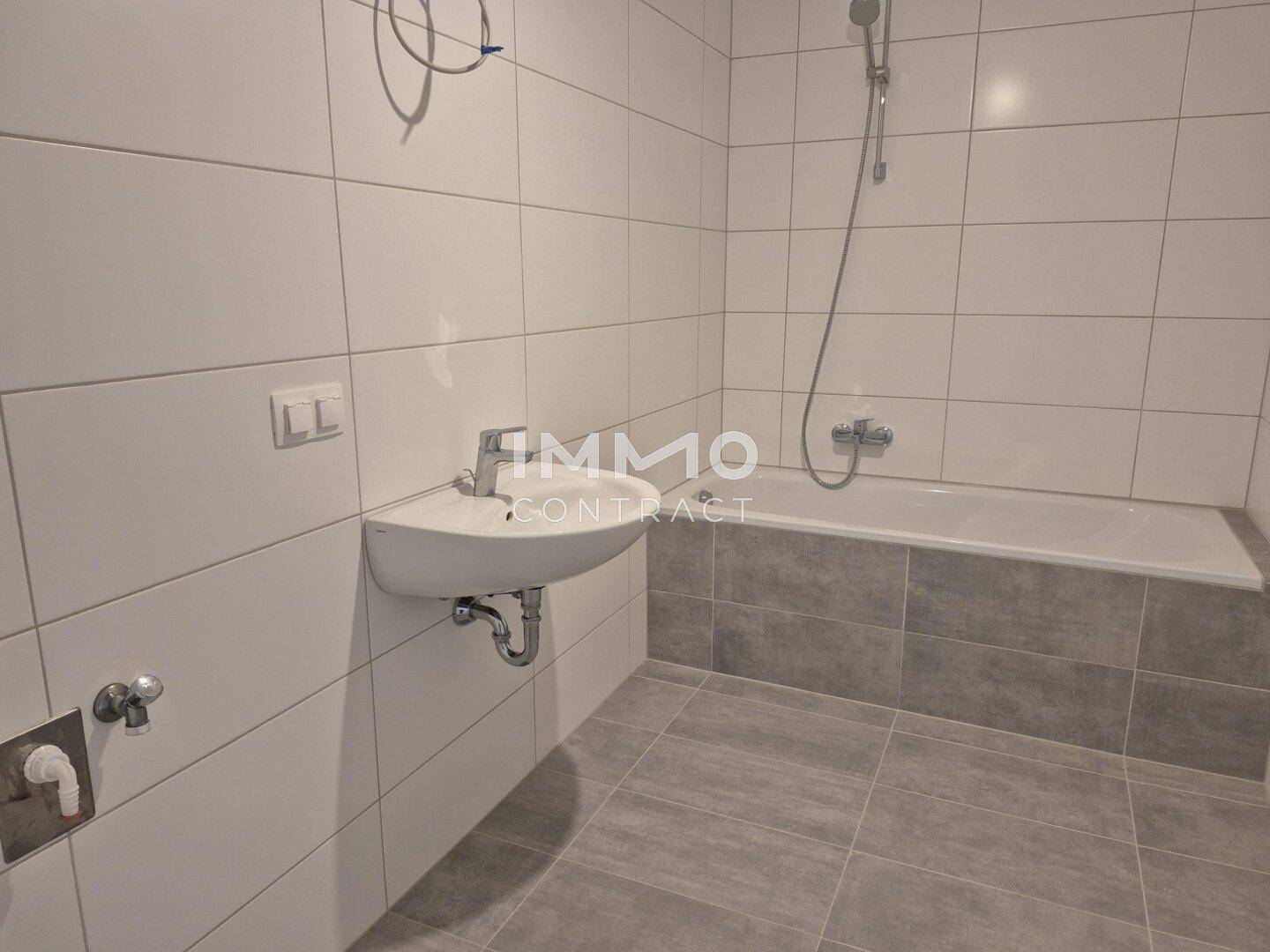 Modernes Badezimmer mit weißen Wandfliesen, grauen Bodenfliesen und Badewanne.