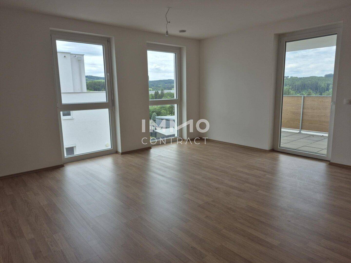Heller Wohnraum mit Laminatboden, großen Fenstern und direktem Zugang zum Balkon.