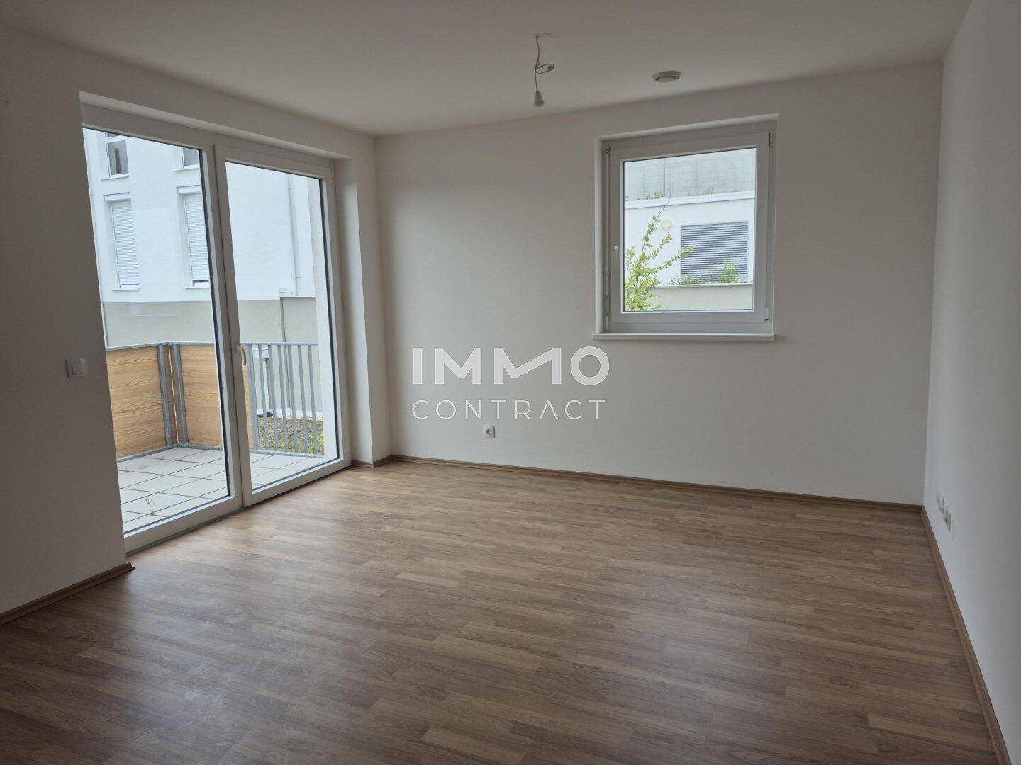 Heller, leerer Raum mit Laminatboden, großen Fenstern und Balkonzugang.