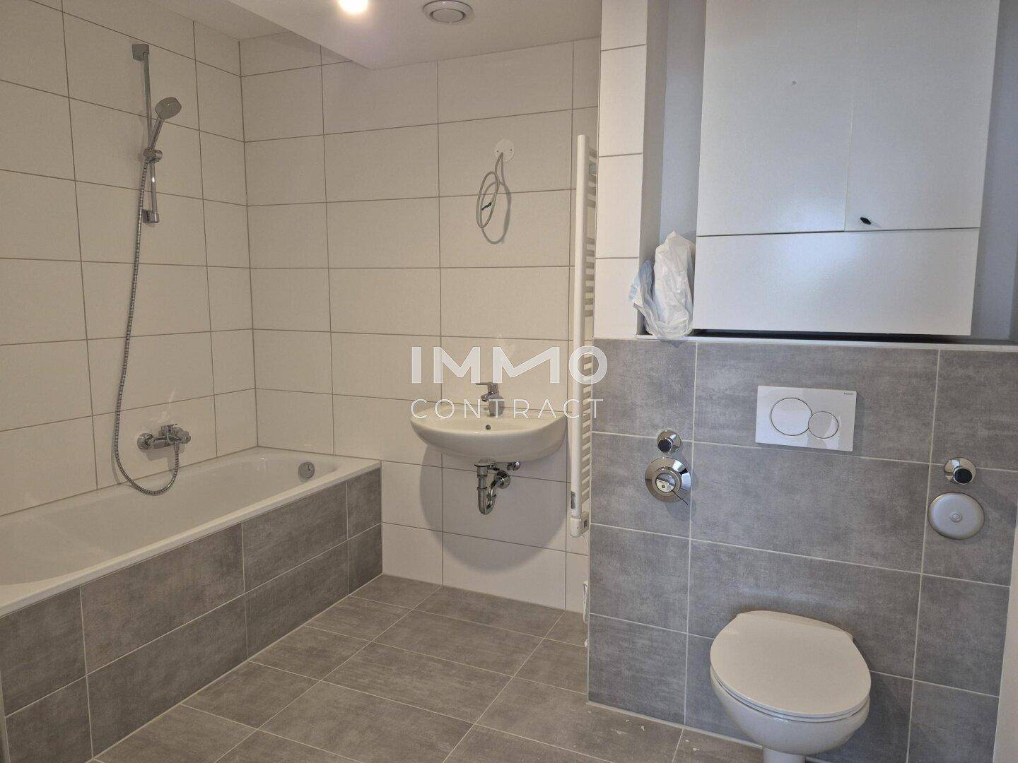 Modernes Badezimmer mit Badewanne, WC, Waschbecken und grauen Fliesen in zeitgemäßem Design.