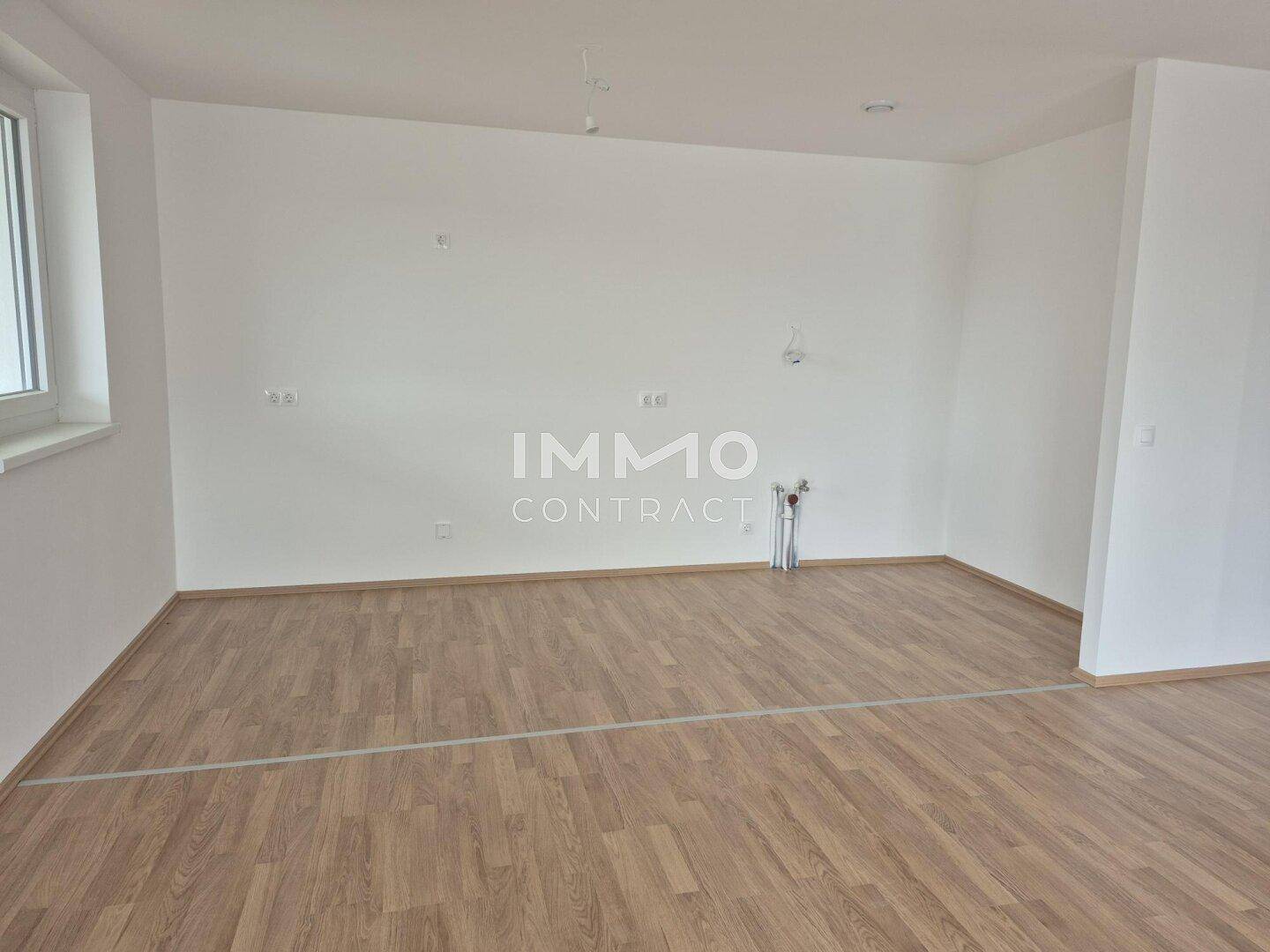 Heller, unmöblierter Wohnraum mit Laminatboden und großem Fenster, ideal für offene Konzepte.