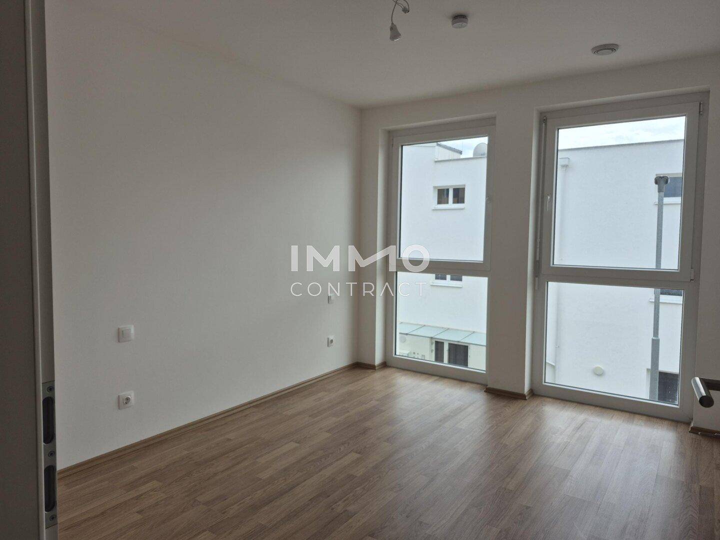 Helles Schlafzimmer mit Laminatboden und großen Fenstern, die viel Tageslicht hereinlassen.