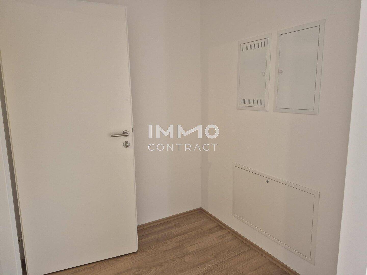 Leerer Flur mit Laminatboden, einer weißen Tür und Wartungsklappen an der Wand.