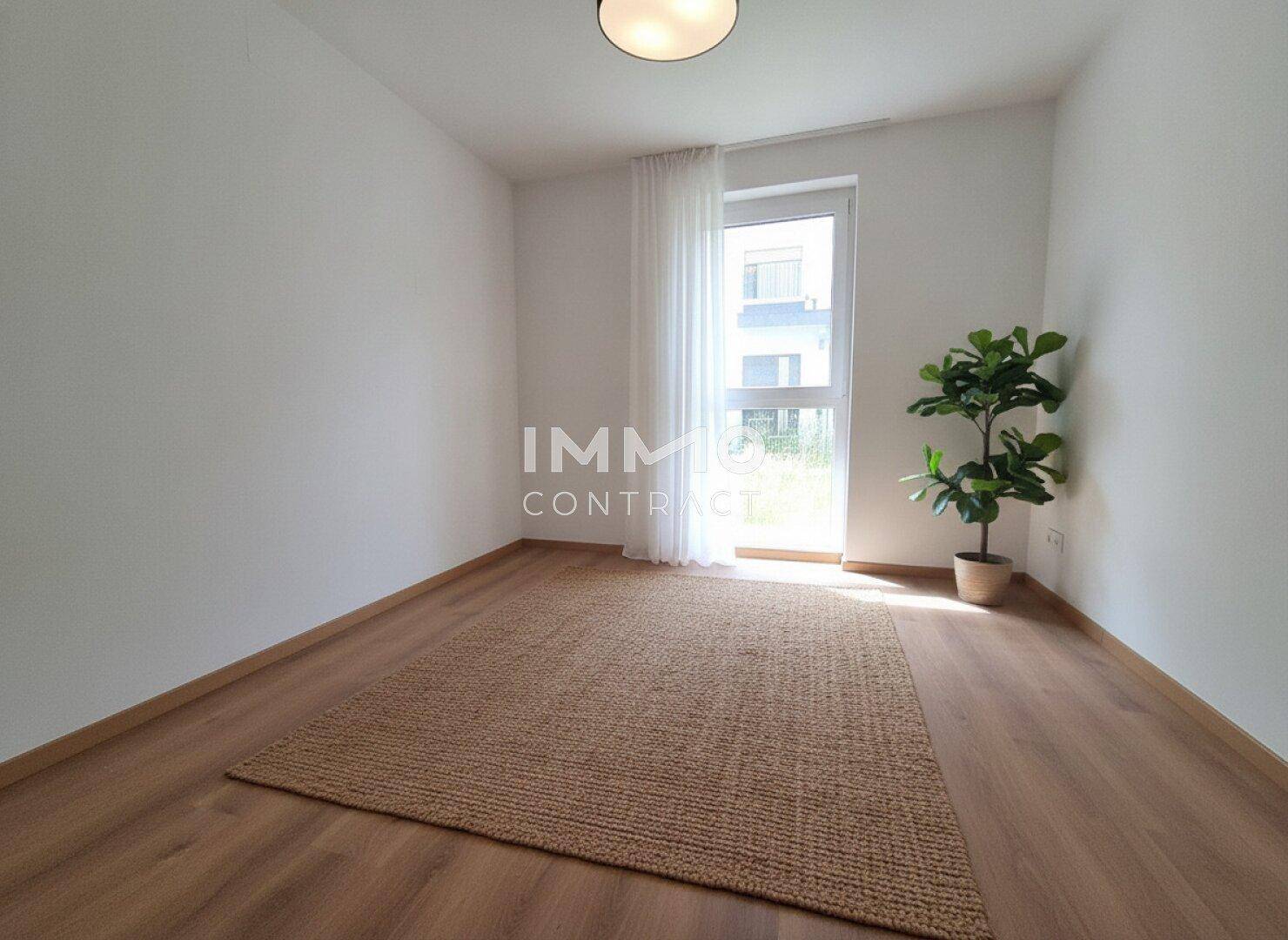 Leeres Zimmer mit Laminatboden, großem Fenster, einer Pflanze und einem Teppich, bereit zur individuellen Gestaltung.