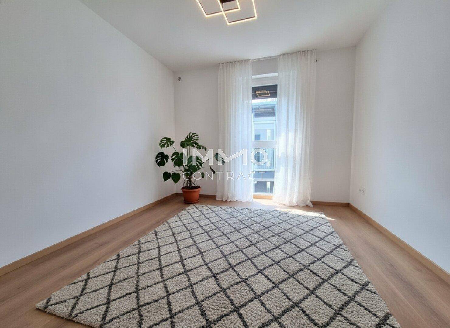 Helles, unmöbliertes Zimmer mit Parkettboden, großem Fenster und moderner Deckenleuchte.