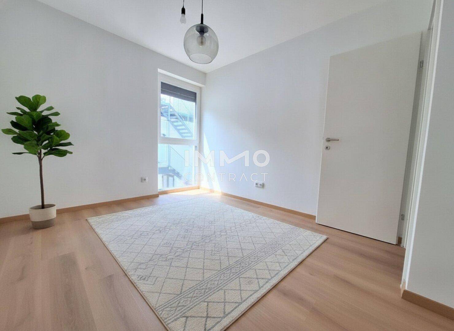 Lichtdurchflutetes Zimmer mit Holzboden, weiß gestrichenen Wänden und Blick nach draußen.
