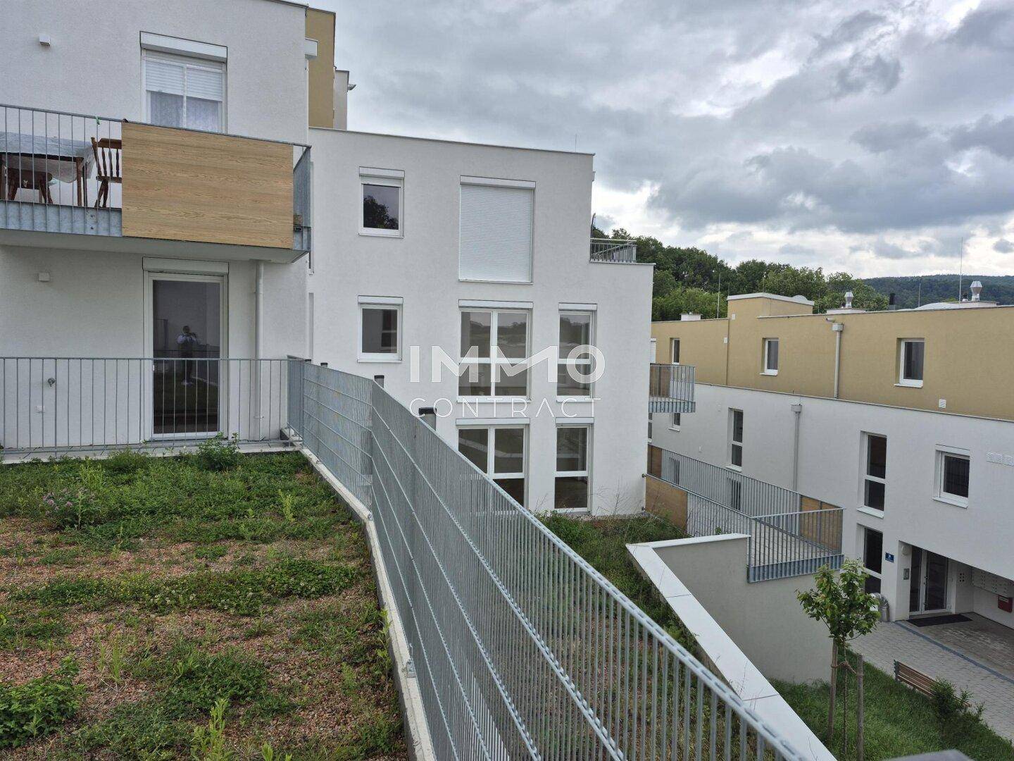 Außenansicht des modernen Apartmentgebäudes mit Balkonen und begrünten Hangflächen.