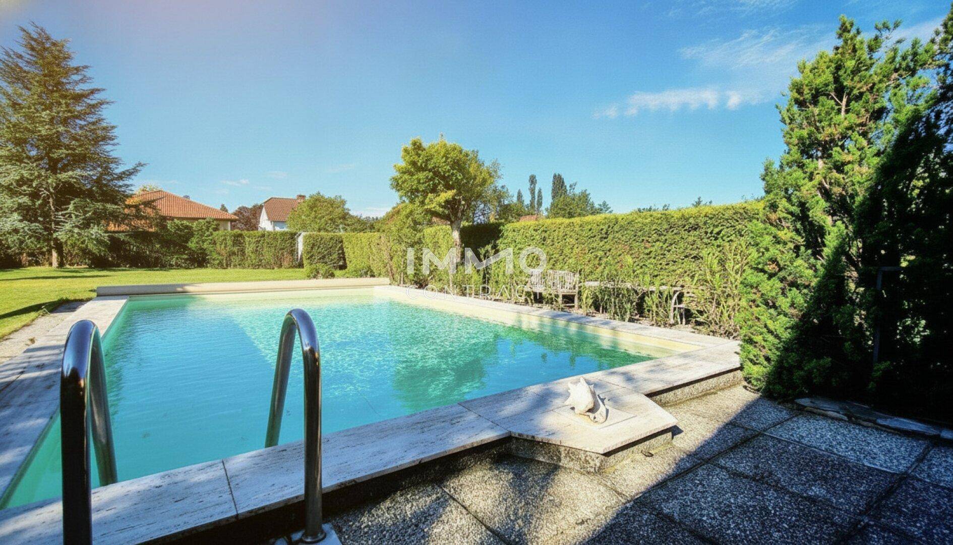 Großzügiger Swimmingpool-Bereich mit gepflasterter Umrandung und hohen Hecken für Privatsphäre.